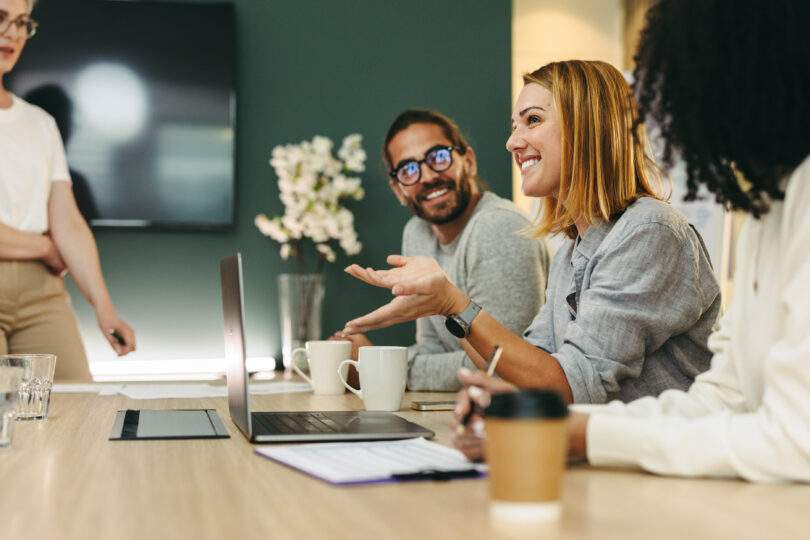 Foto: Eine Geschäftsfrau unterhält sich während einer Besprechung im Sitzungssaal mit ihren Kollegen. Eine Gruppe fröhlicher Geschäftsleute arbeitet gemeinsam in einem kreativen Büro. (c) iStock.com/jacoblund